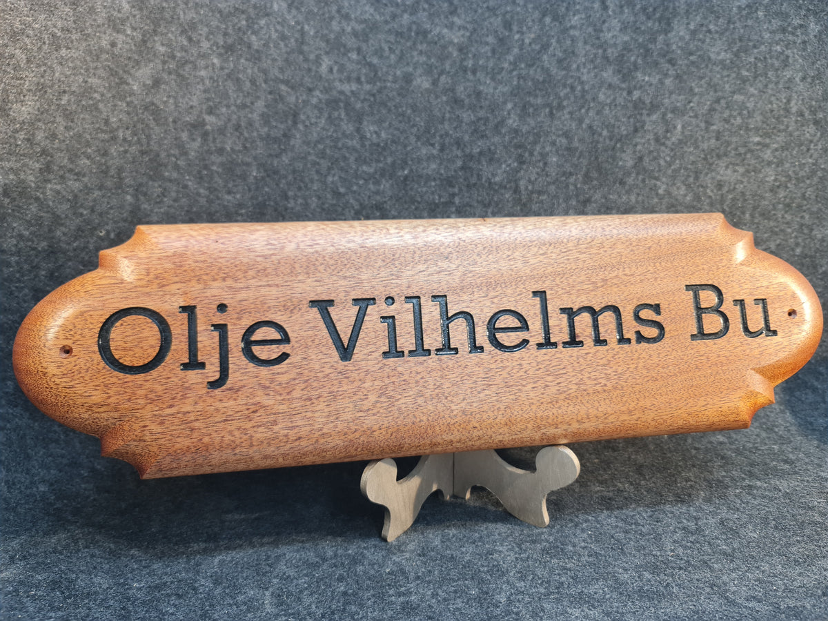 Detaljrik namnskylt i massivt trä med kursiv text, handtillverkad design för en personlig touch på husvagnen.