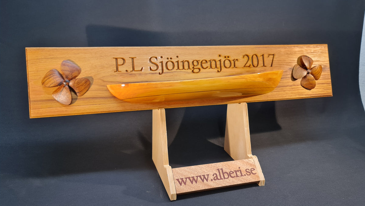 Handgjord minnesskylt i massiv teak med 3D-relief av ett gult fartygsskrov och propellrar från Alberi.