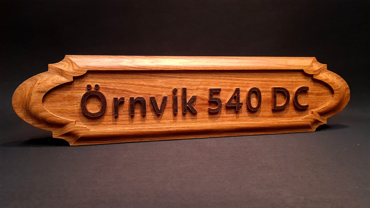Personlig namnskylt "Örnvik 540 DC" i ädelträ ek med tydlig relieftext, skapad för marin miljö.